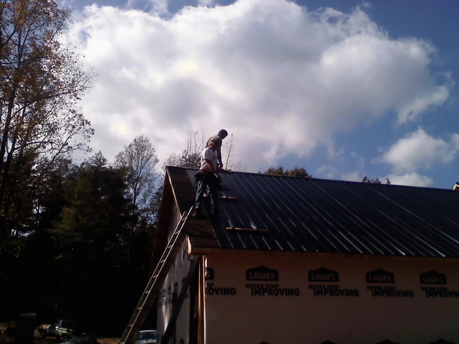 Roofer fastening dark metal panels high against a cloudy sky, from a Roof Inspection job in Logan