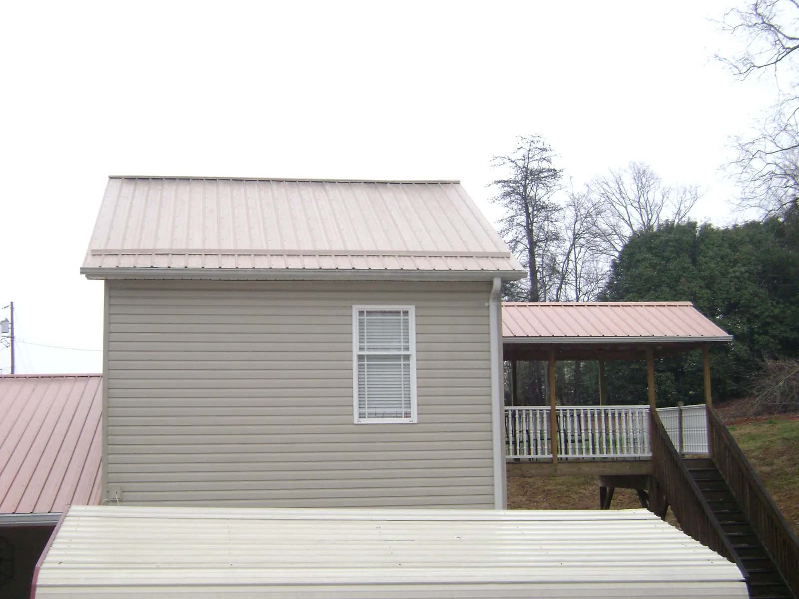 Tan metal roofs on a two story addition and attached porch, from a Roof Replacement job in Logan